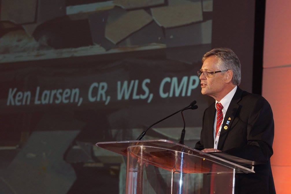 Ken Larsen speaking at a lectern during a professional presentation